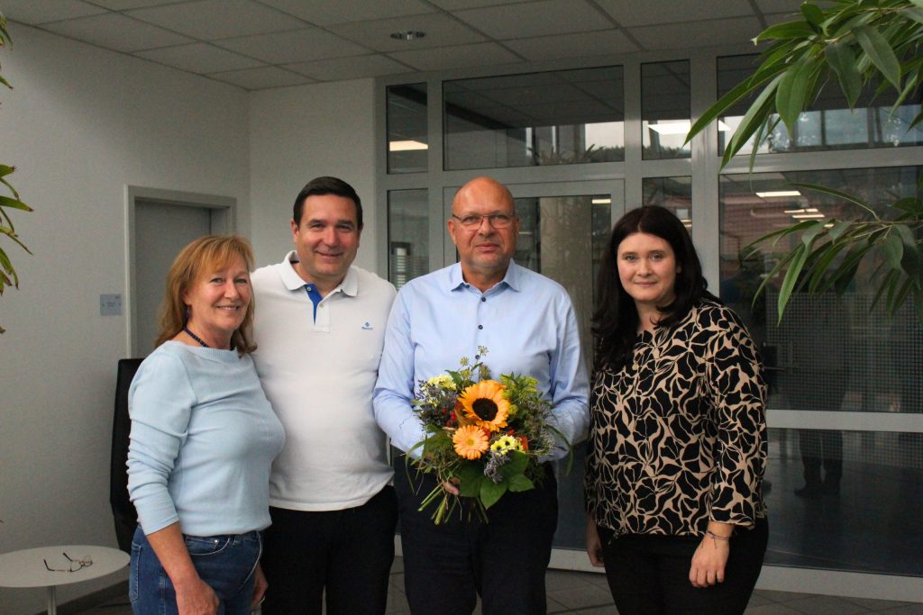 Andrea Hädrich, Christian Franke und Anja Eckardt gratulieren Olaf Skarke mit einem Blumenstrauß